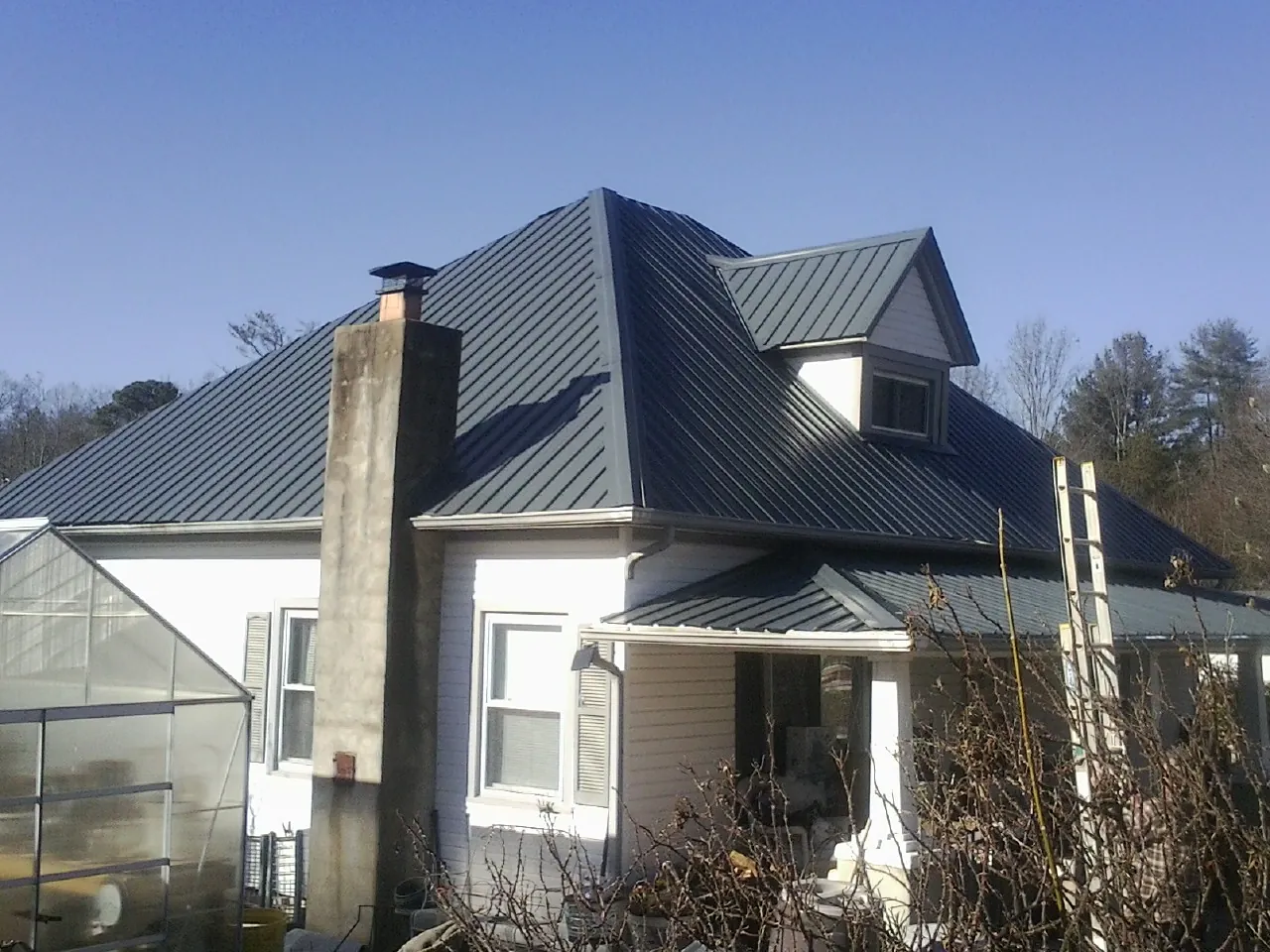 Dark blue standing seam metal roof on a white farmhouse with dormer — Slate & Tile Roof Repair by Roofing Brothers in Micanopy