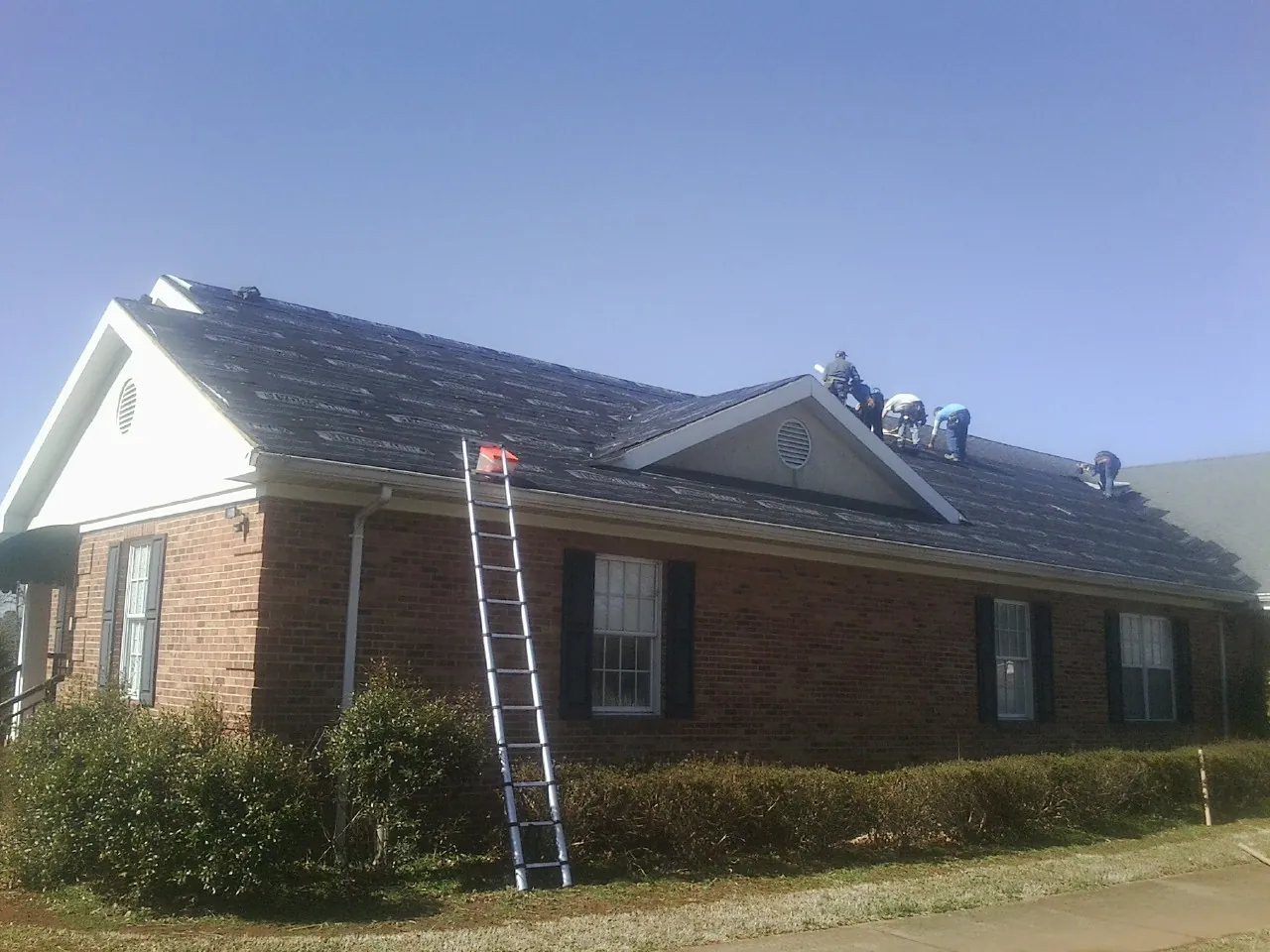 Crew tearing shingles off a brick ranch roof with a ladder set — Emergency Roof Repair work by our crew in Micanopy