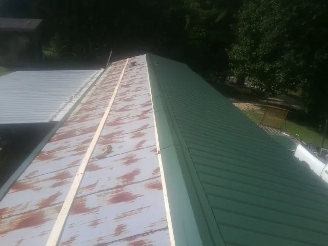 Old rusted panels beside newly installed green metal roofing — Wind Damage Roof Repair by Roofing Brothers in Micanopy