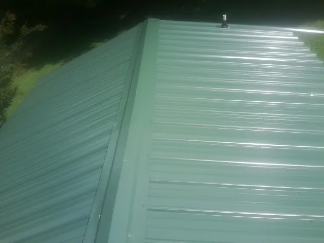 New green metal panels meeting at the ridge of a roof — Flat Roof Repair work by our crew in Micanopy