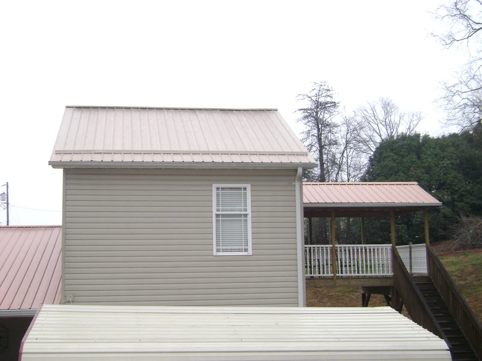 Tan metal roofs on a two story addition and attached porch, from a Roof Replacement job in Micanopy